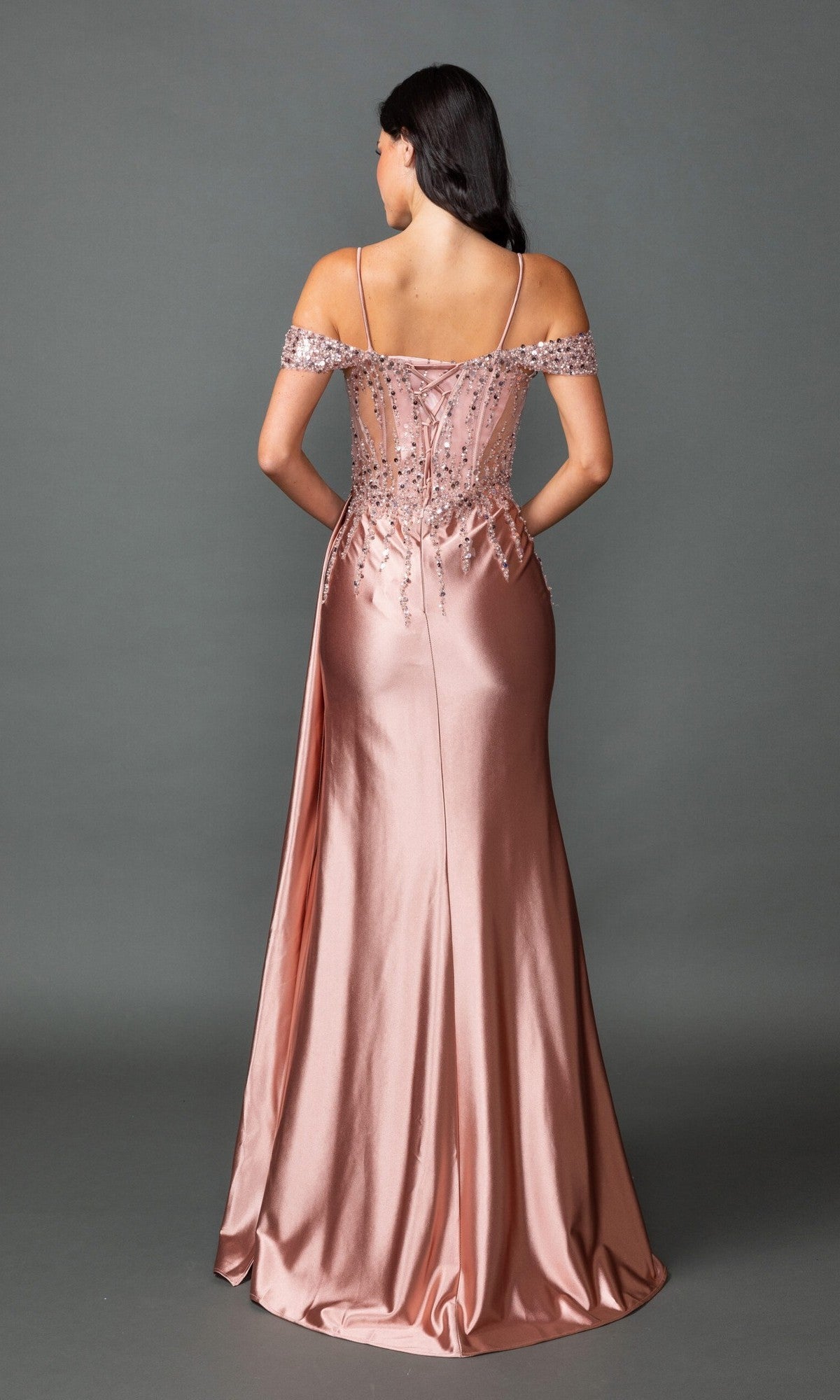 A woman faces away, wearing the Dancing Queen 4551 long prom dress in blush pink with off-the-shoulder style, sequin embellishments, and lace-up back, set against a plain gray background.
